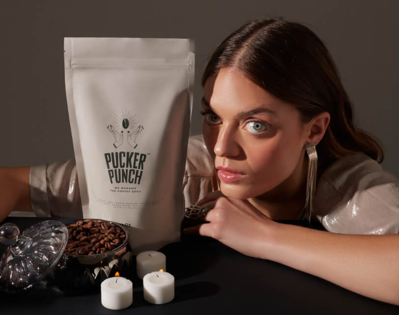 Woman next to a Pucker Punch coffee package with coffee beans and candles